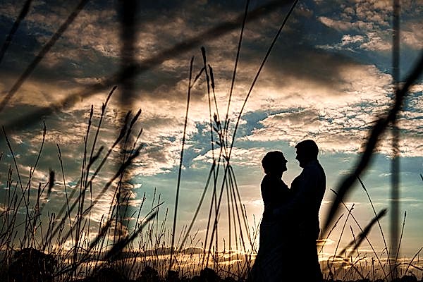 Silhouetted couple in field at sunset.