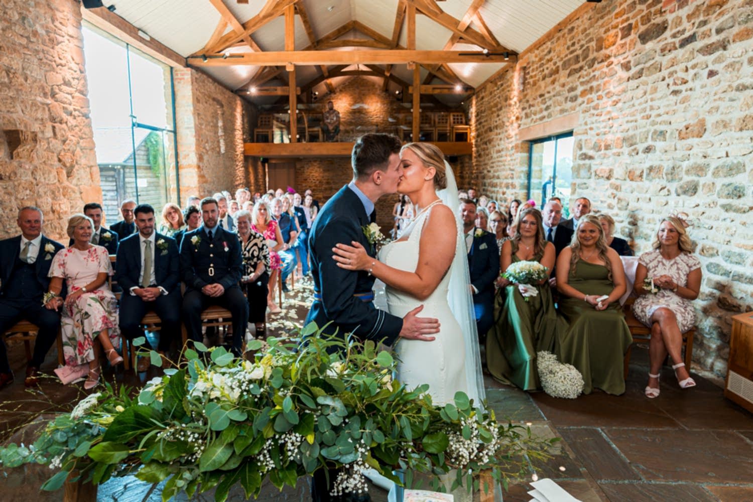 Couple kissing at wedding ceremony in rustic venue.