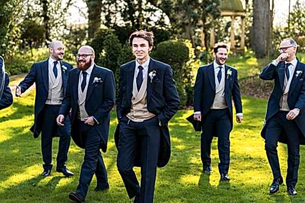 Groomsmen in suits walking in a garden.