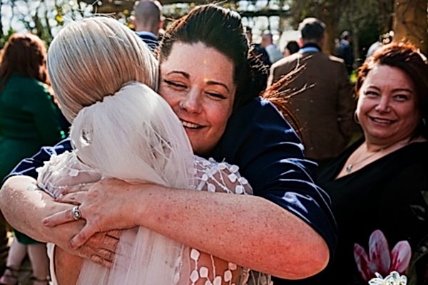 Wedding guests hugging outdoors under the sun.