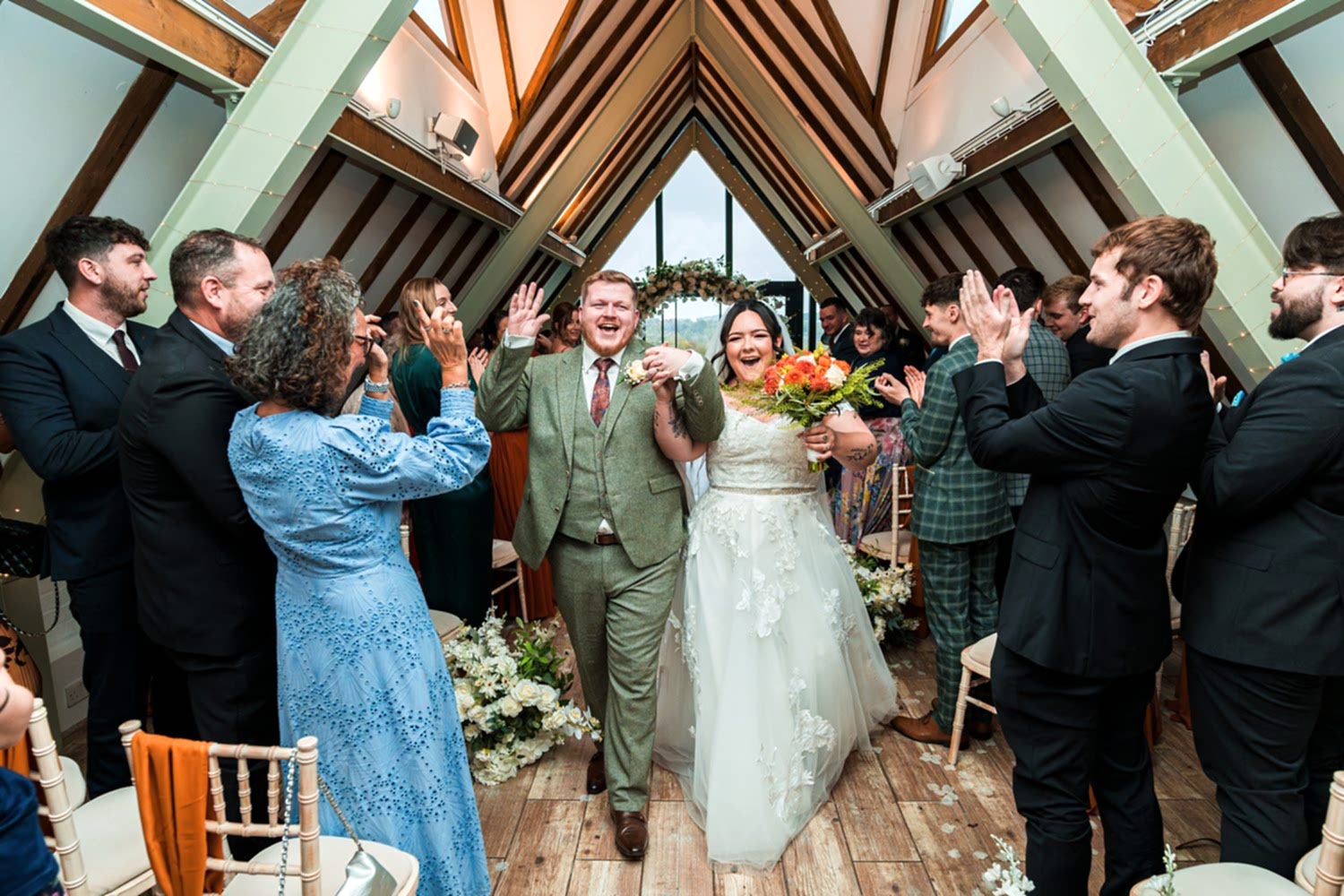 Newlyweds celebrate surrounded by clapping guests indoors.