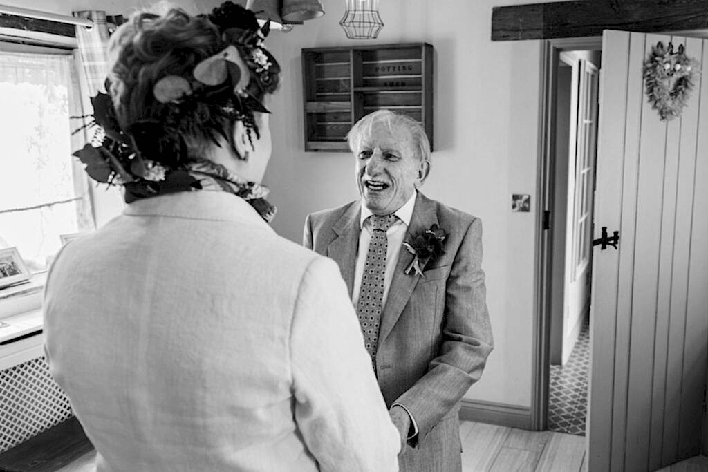 Smiling elderly man in suit with boutonniere indoors.