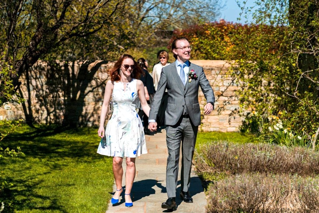 Couple walking in garden path, holding hands, laughing.