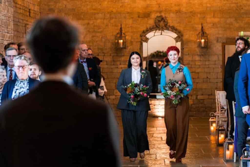 Two people walking down wedding aisle with flowers.