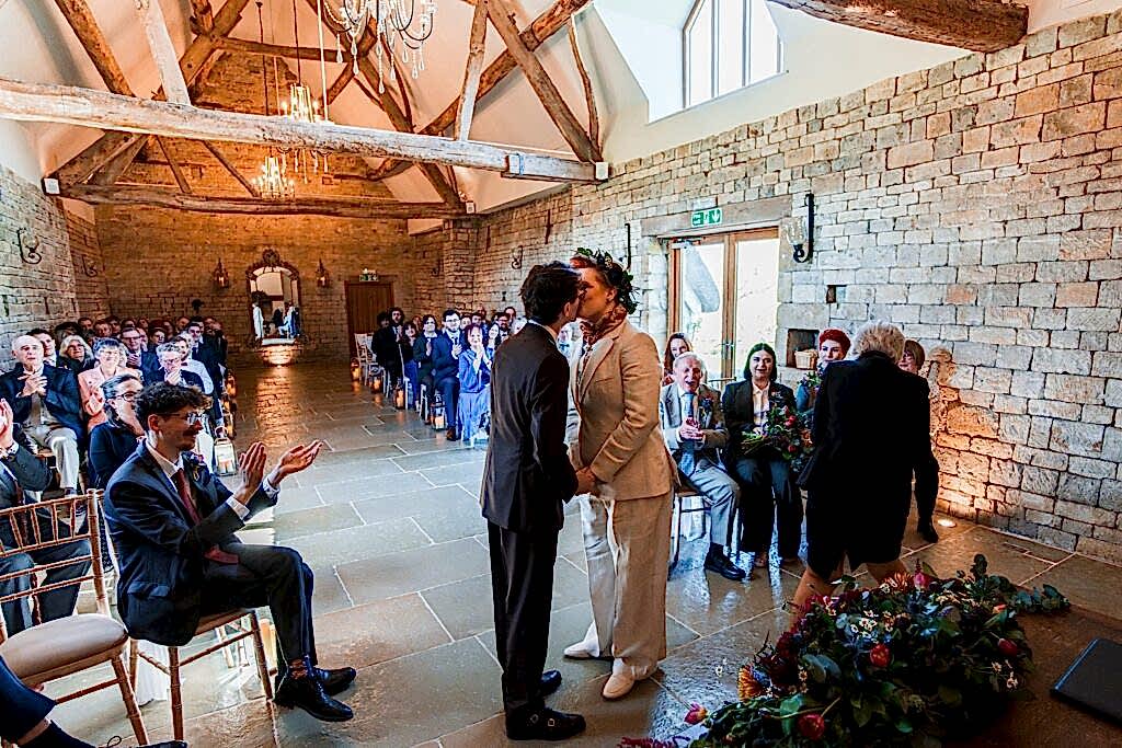 Couple kissing at wedding ceremony in rustic venue.