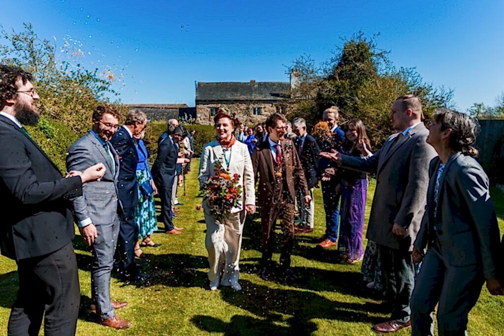 Wedding couple walks through confetti and cheering guests.