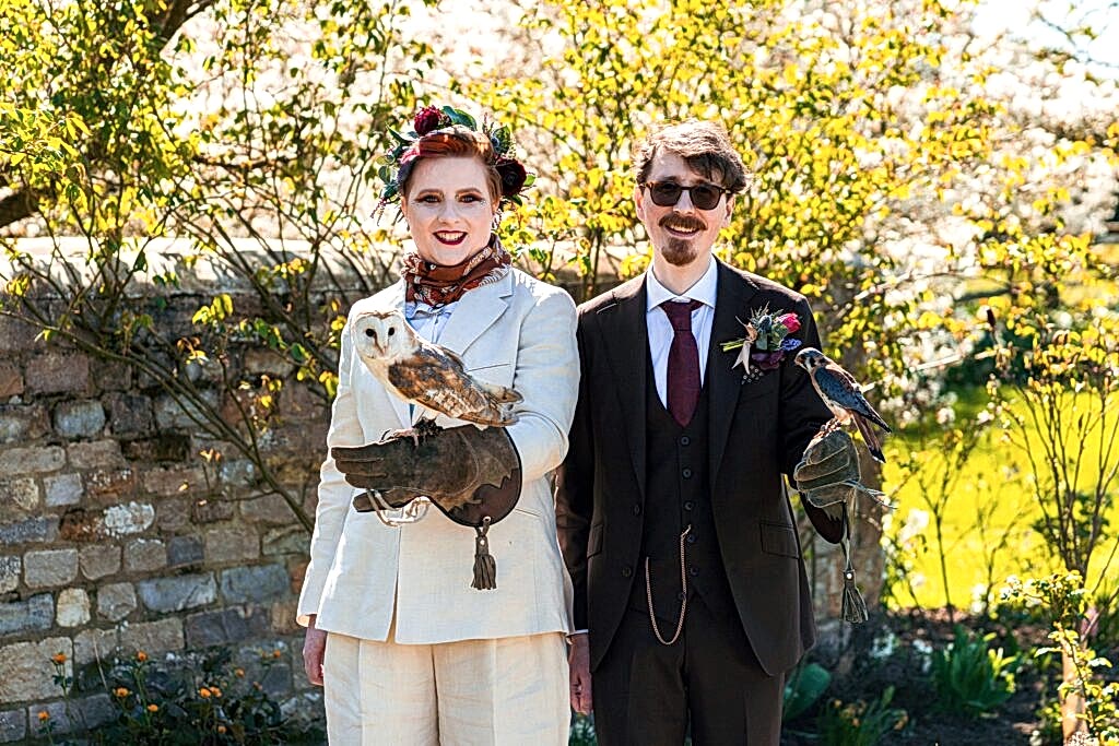 Couple dressed with birds on arms, outdoor setting.