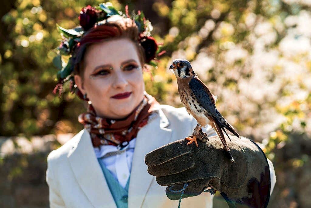 Person holding falcon in garden setting.