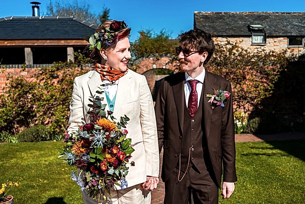 Smiling couple holding hands outdoors, colourful bouquet.