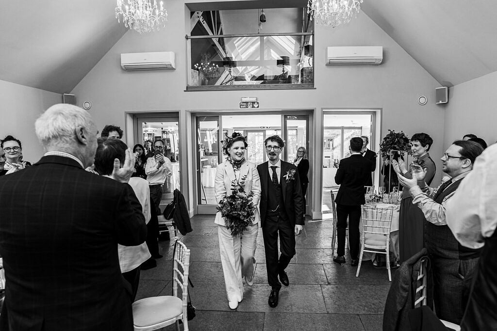 Newlyweds walk down aisle, guests applaud.