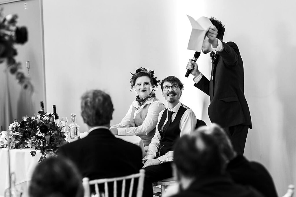 Wedding speech with bride and groom seated, smiling.