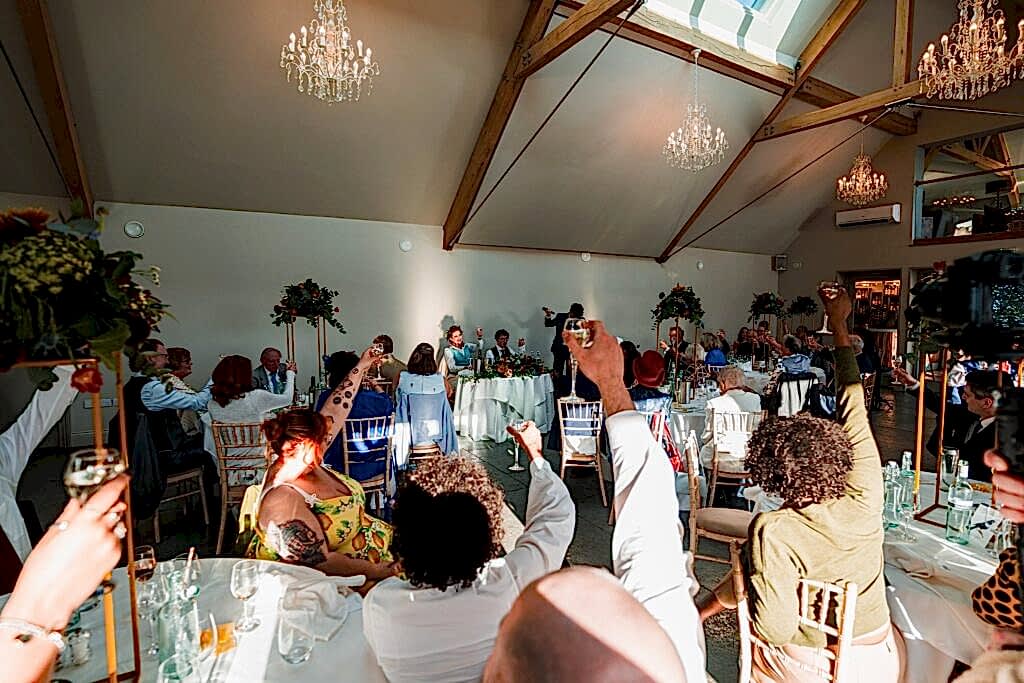 Guests raising glasses at a wedding reception toast.