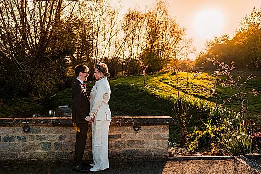 Couple holding hands on a sunny countryside bridge.