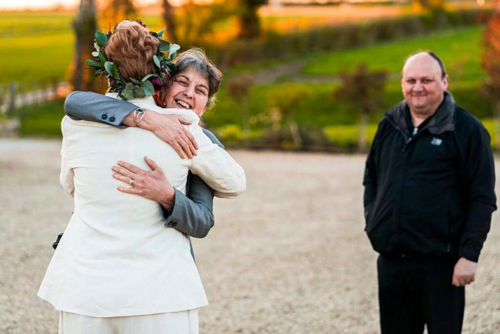 Happy people embracing outdoors with smiling onlooker.