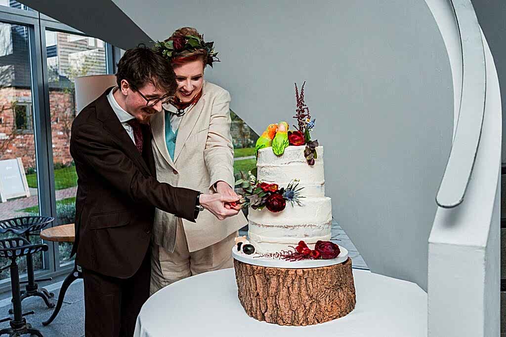Couple cutting rustic wedding cake together indoors.