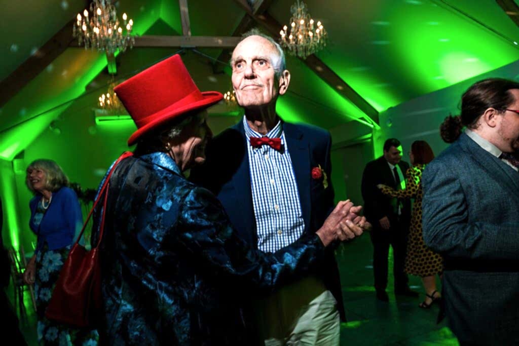 Elderly couple dancing at a party with green lights.