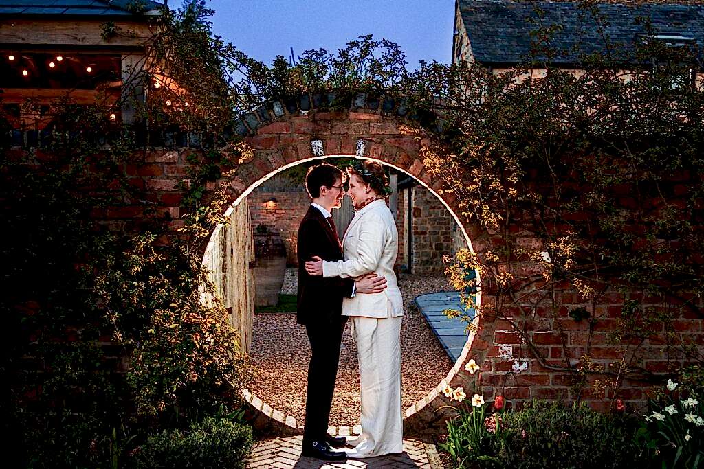 Couple embracing under brick garden archway.