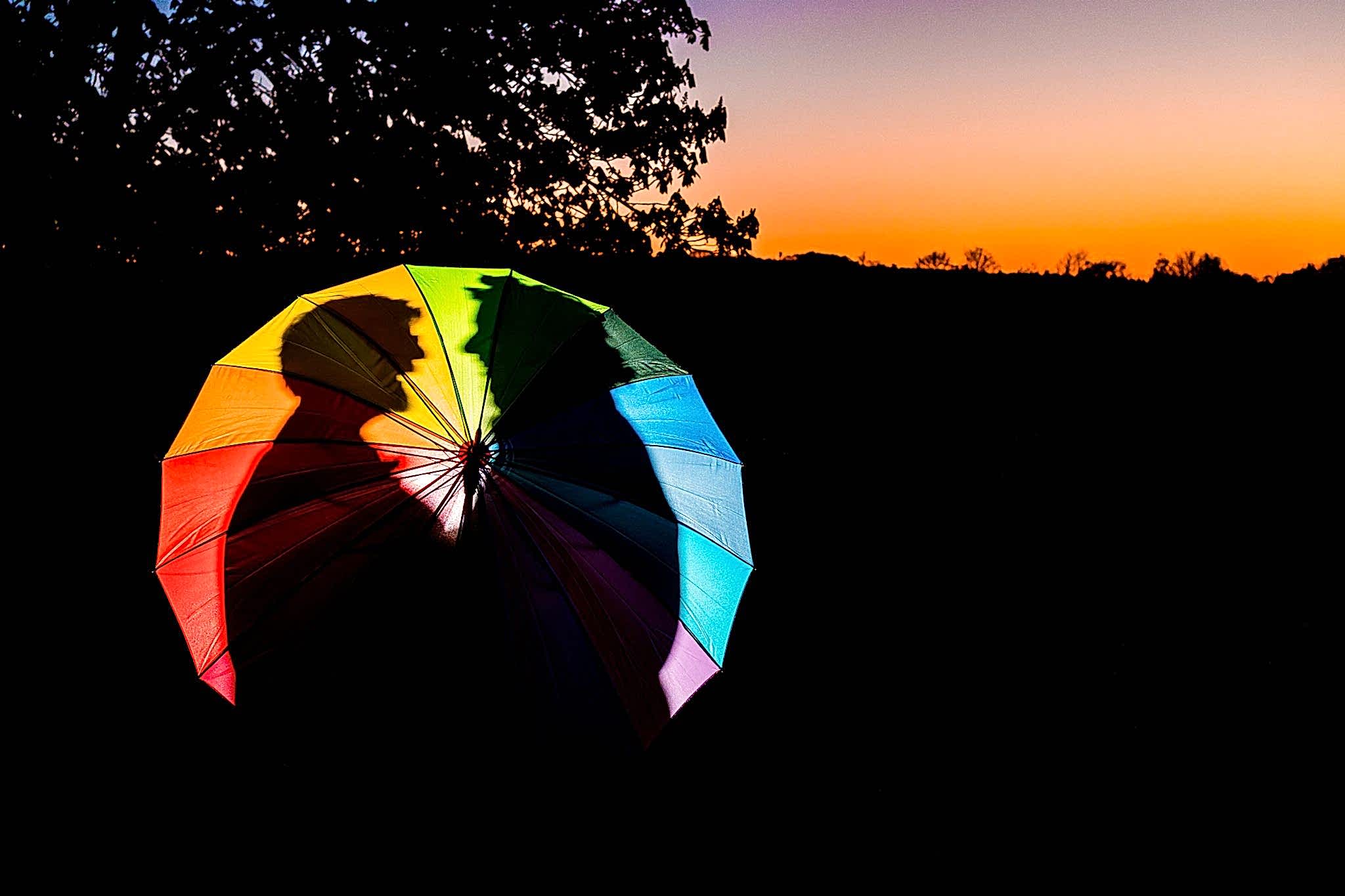 Silhouette behind a colourful umbrella at sunset.