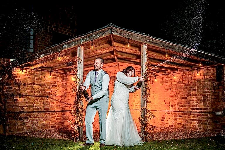 Couple celebrate with champagne under rustic shelter.