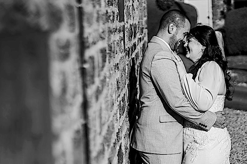Smiling couple embrace by stone wall, wedding day.