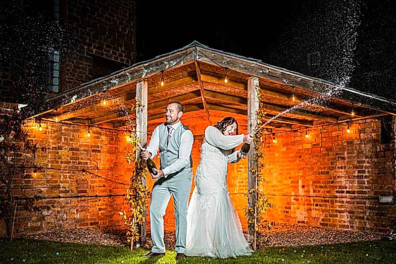 Bride and groom celebrating with champagne outside marquee.