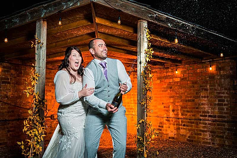 Couple celebrating with champagne at rustic venue.