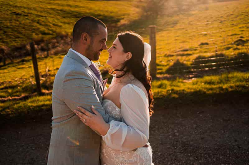 Couple embracing in countryside, sunlight behind.