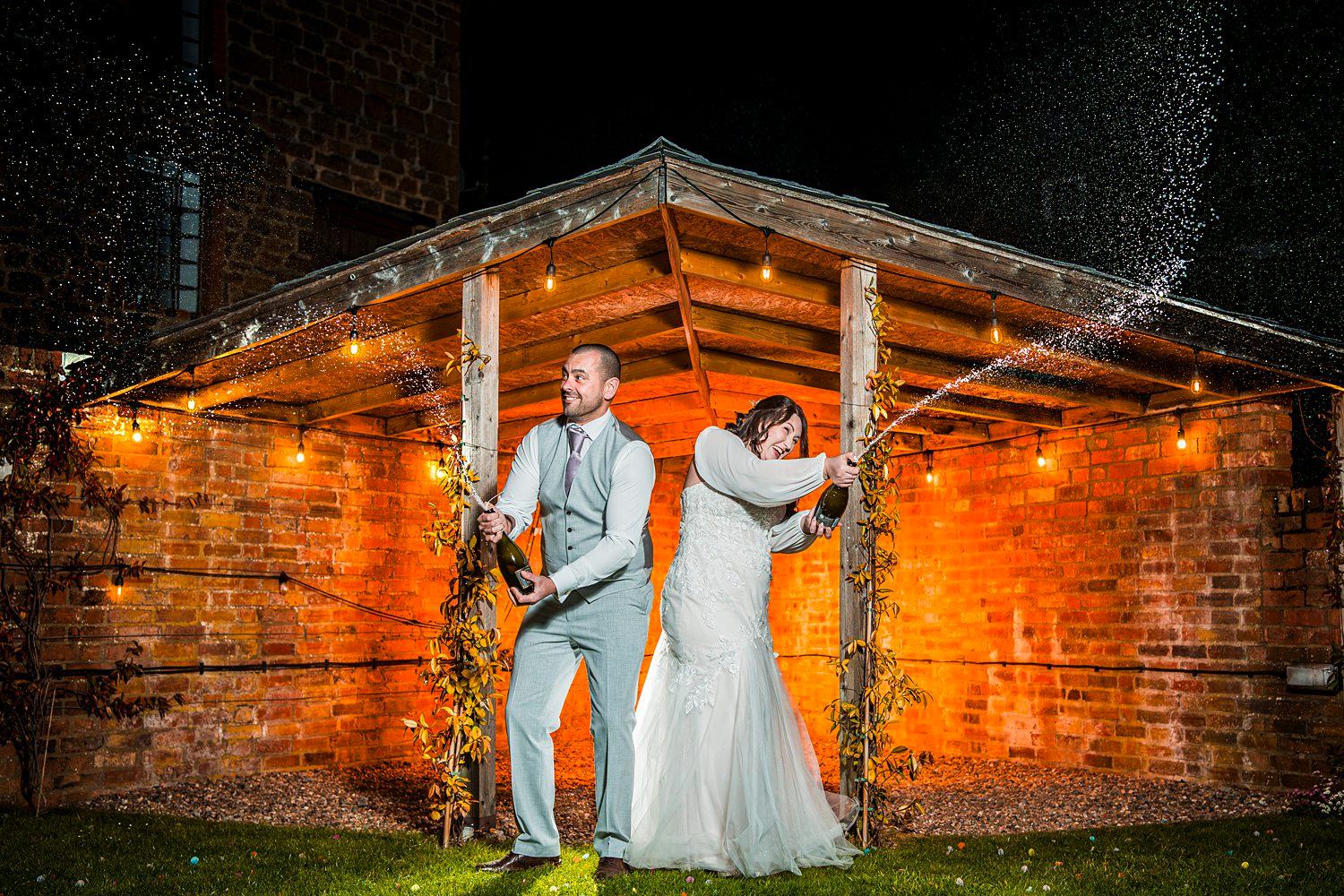 Couple celebrate with champagne under rustic shelter.